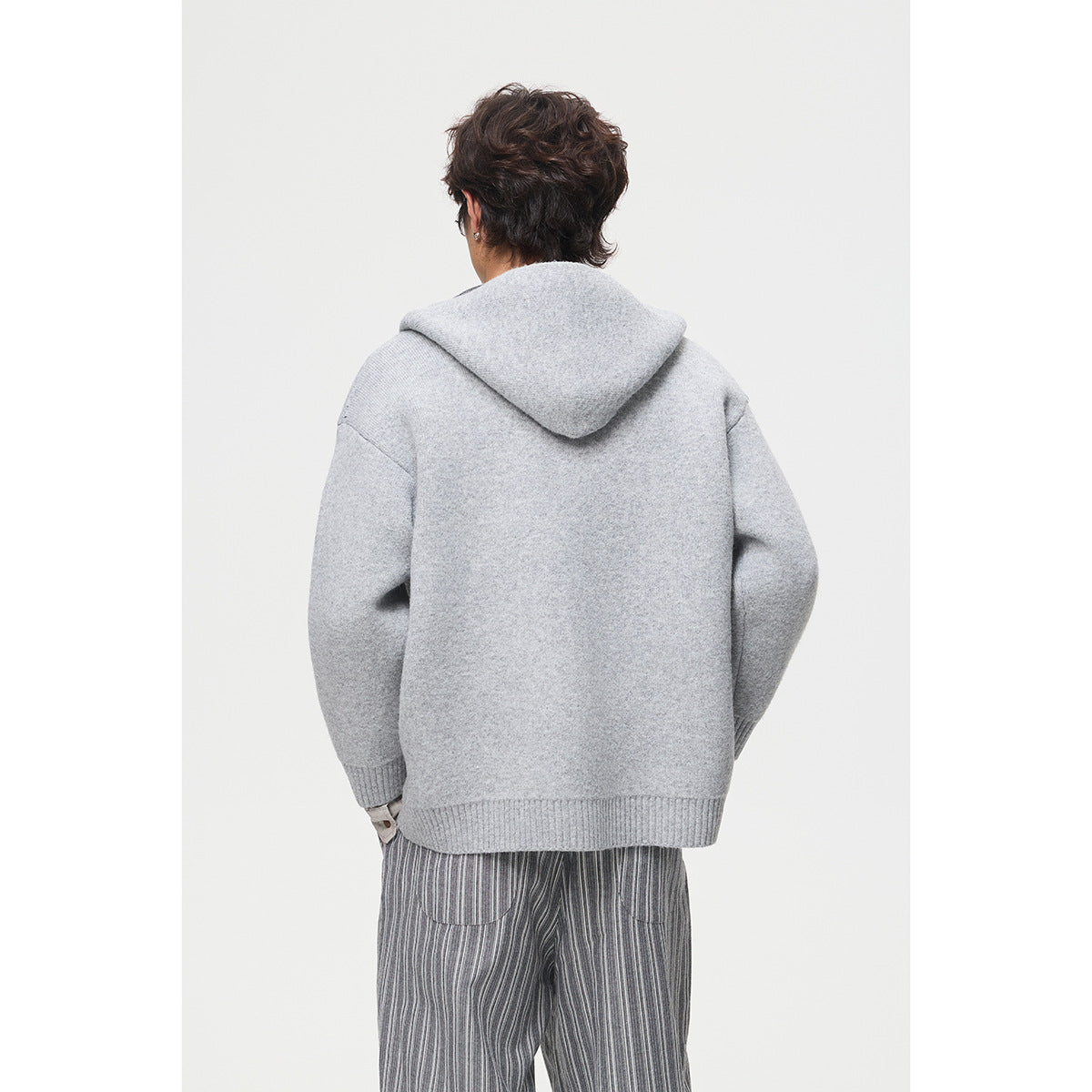 Back view of a model wearing a light gray hooded knit jacket with ribbed cuffs and hem.