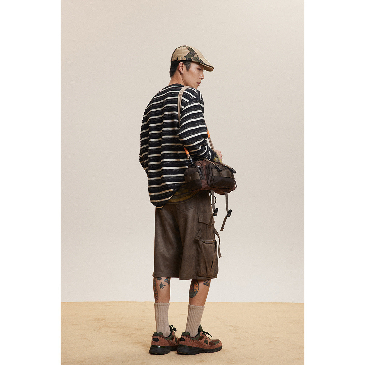 Model in a black-and-white striped long-sleeve shirt and brown cargo shorts, viewed from behind with a shoulder bag.