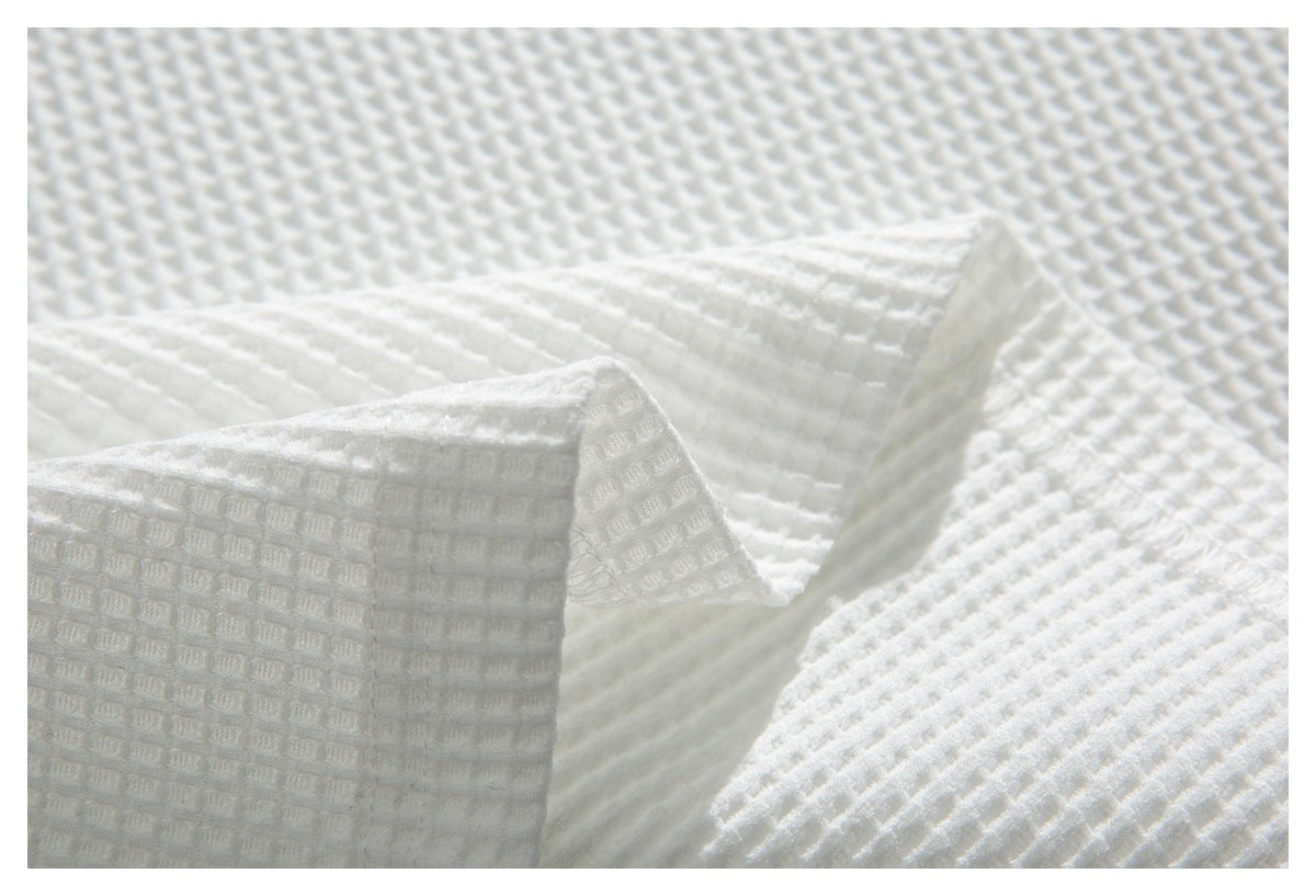 Close-up of white waffle-textured fabric showing a folded seam and stitched edge.