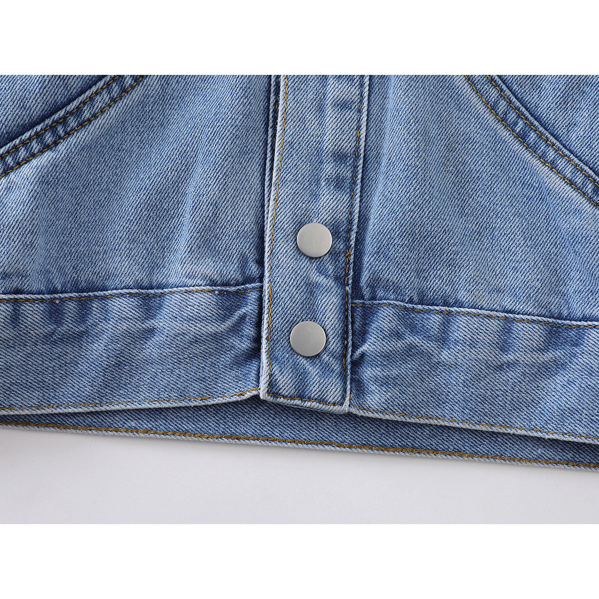 Close-up of the light blue denim jacket’s lower front, showing the snap-button placket and curved seams.