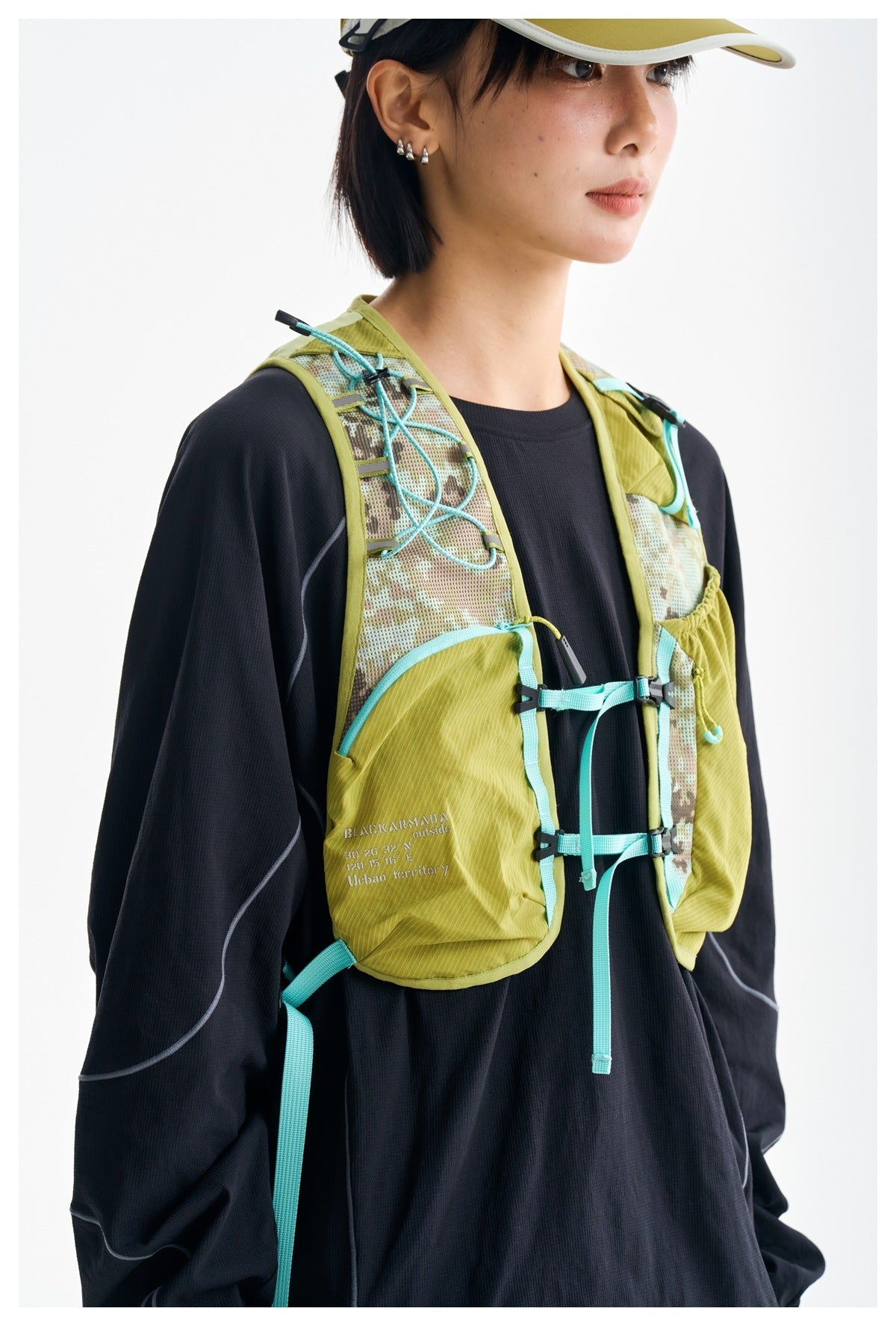 Close front view of an olive hiking vest with patterned mesh panels, turquoise cords, buckles and pockets.