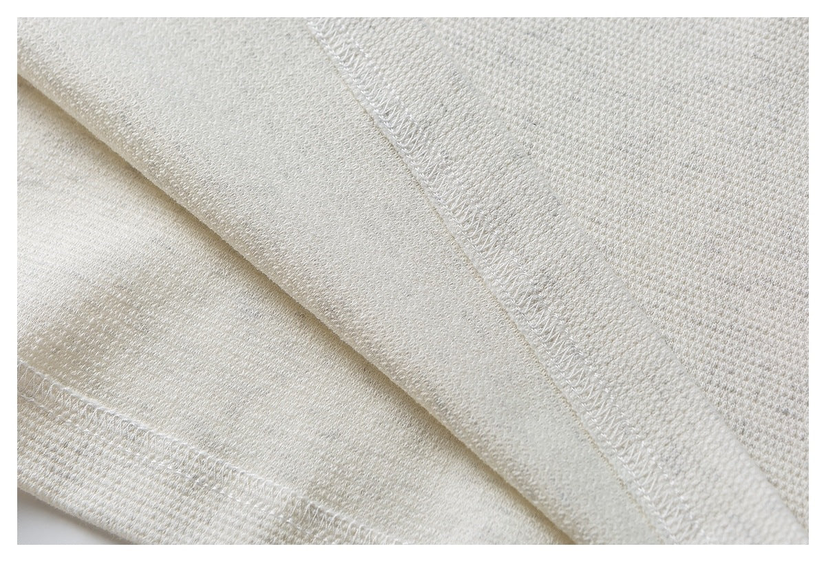 Close-up of off-white fabric showing a fine textured knit and overlocked seam stitching.