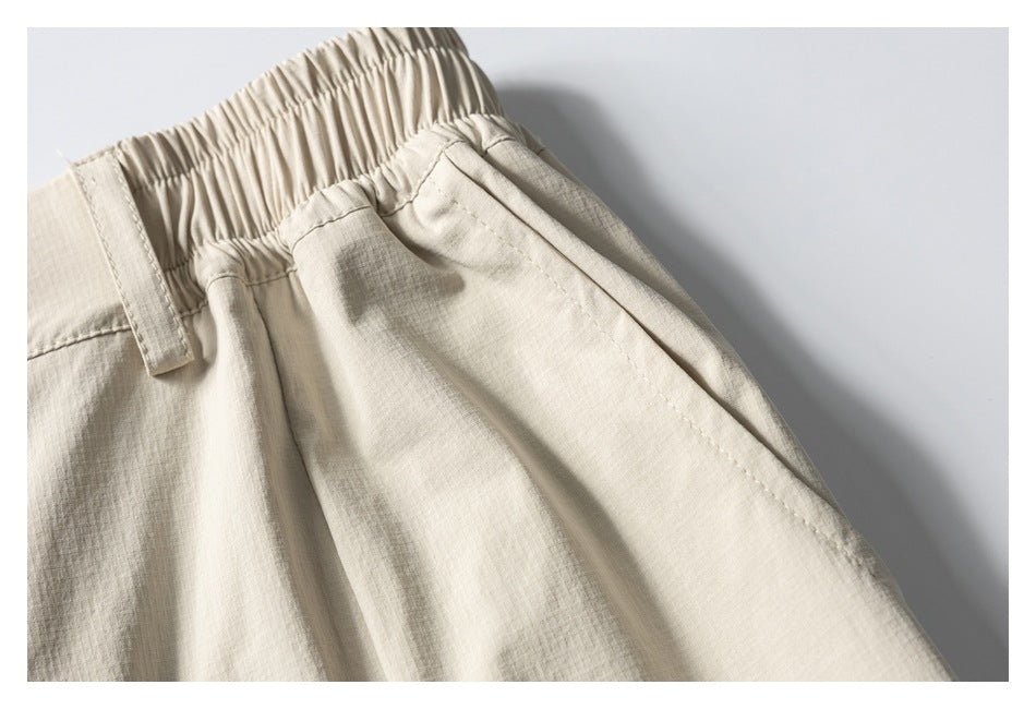 Close-up of light beige trousers showing the gathered elastic waistband, belt loop, and angled pocket opening.