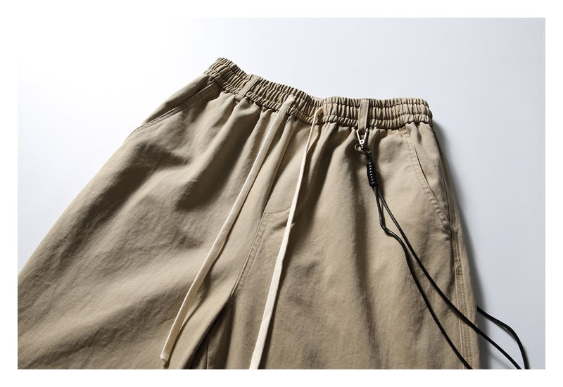 Cropped flat-lay view of khaki trousers with an elastic waistband, light drawstrings and a black cord detail.