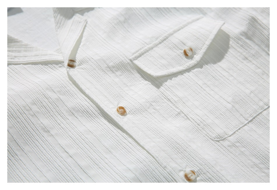 Close-up of a white textured shirt front with tan buttons and a buttoned chest pocket.