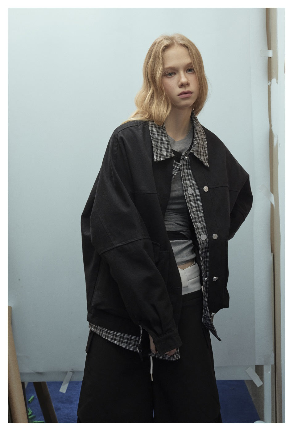 Closer view of a model wearing a black oversized jacket with a plaid collar and placket over a gray top.