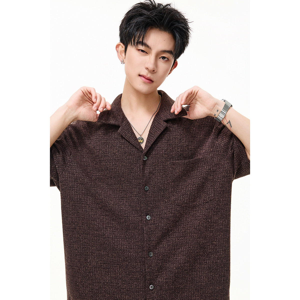 Close view of a model wearing a brown textured short-sleeve shirt with a notched collar, buttons, and chest pocket.