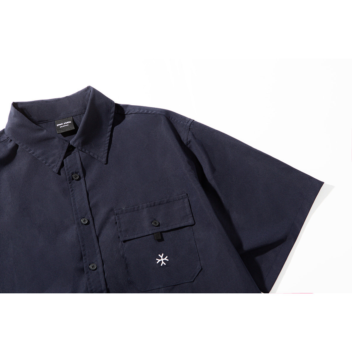 Close-up of a dark navy short-sleeve shirt with a buttoned chest pocket and small embroidered symbol.