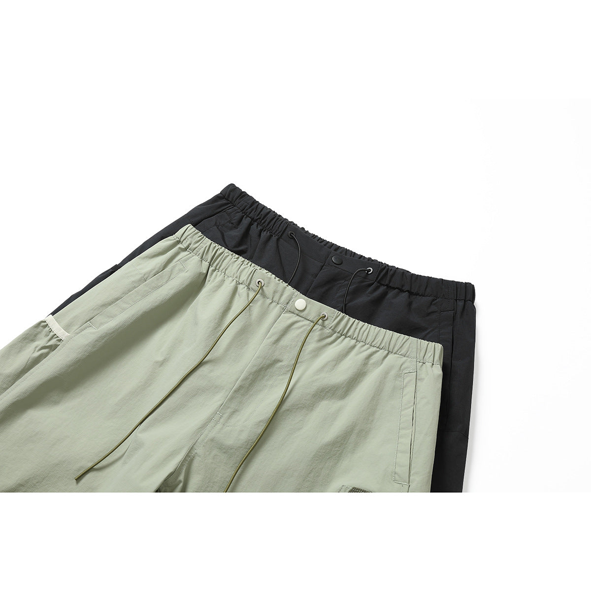 Close-up of black and pale sage-green pants showing elastic waistbands, drawcords, buttons and pockets.