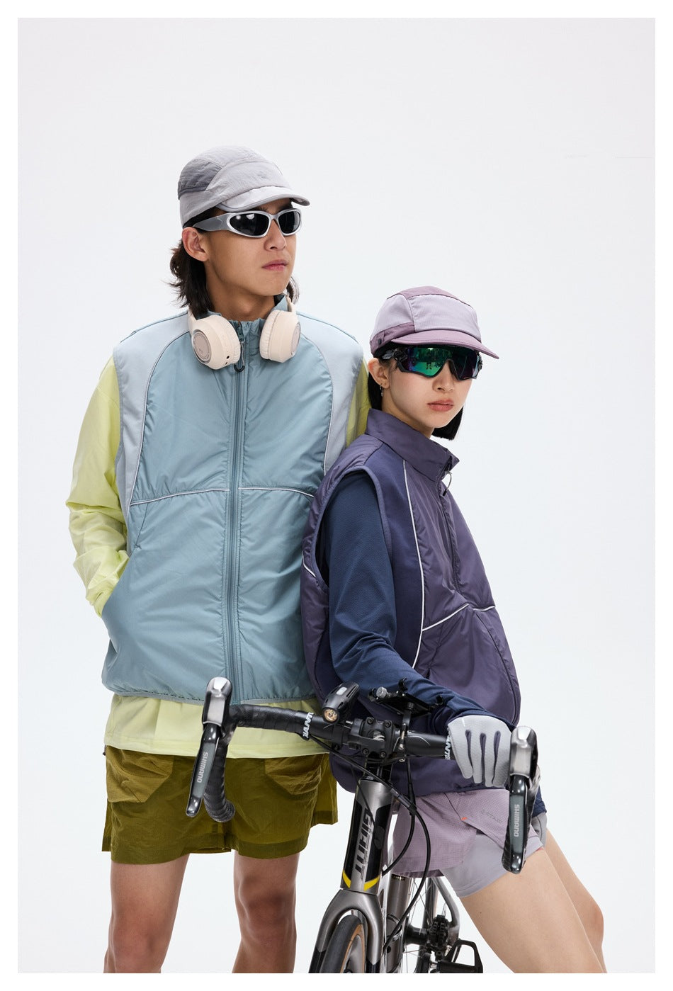 Two cyclists pose in a pale blue and a purple zip-front vest with reflective piping.