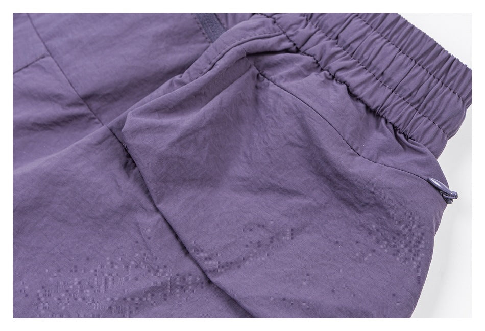 Close-up of purple pants showing the gathered elastic waistband and a side pocket with a small toggle.