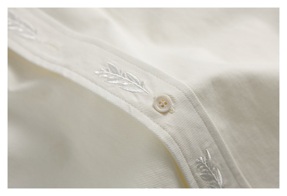 Close-up of an ivory button and small embroidered leaf motifs along a garment placket.