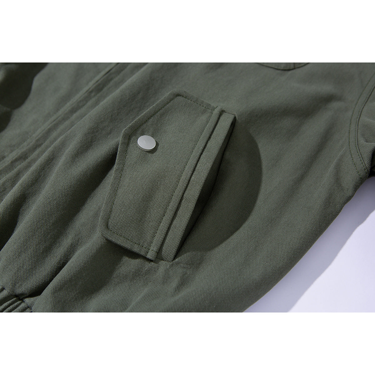 Close-up of an olive jacket's flap pocket with a silver snap button and surrounding seams.