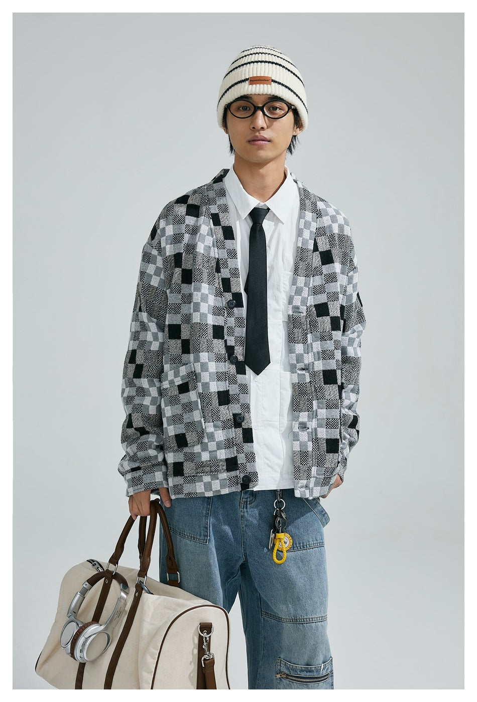 Front view of a model wearing a black, gray and white patchwork-check cardigan with a white shirt and black tie.