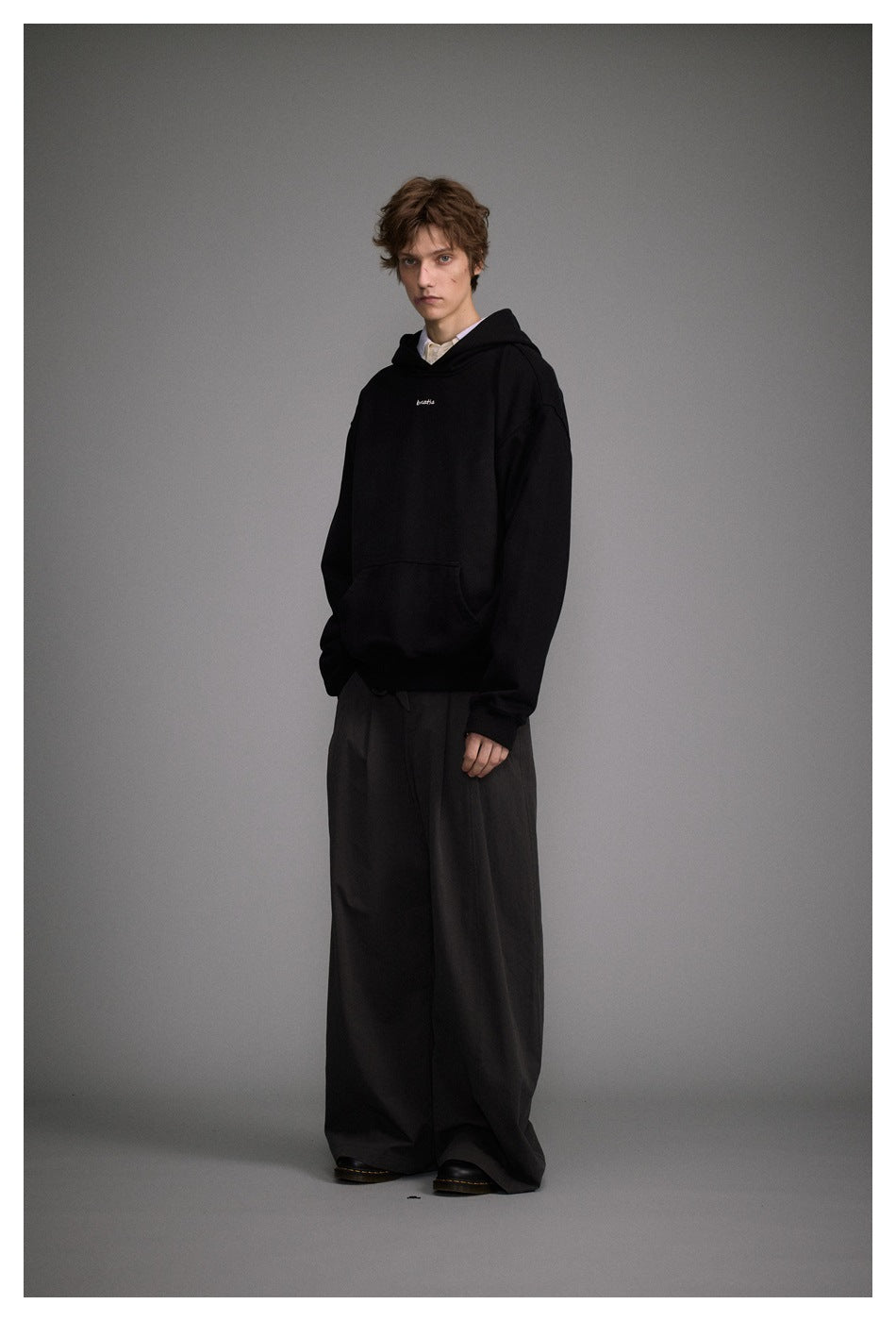 Full-length view of a model in a black hoodie and wide-leg dark trousers with black shoes, standing at an angle