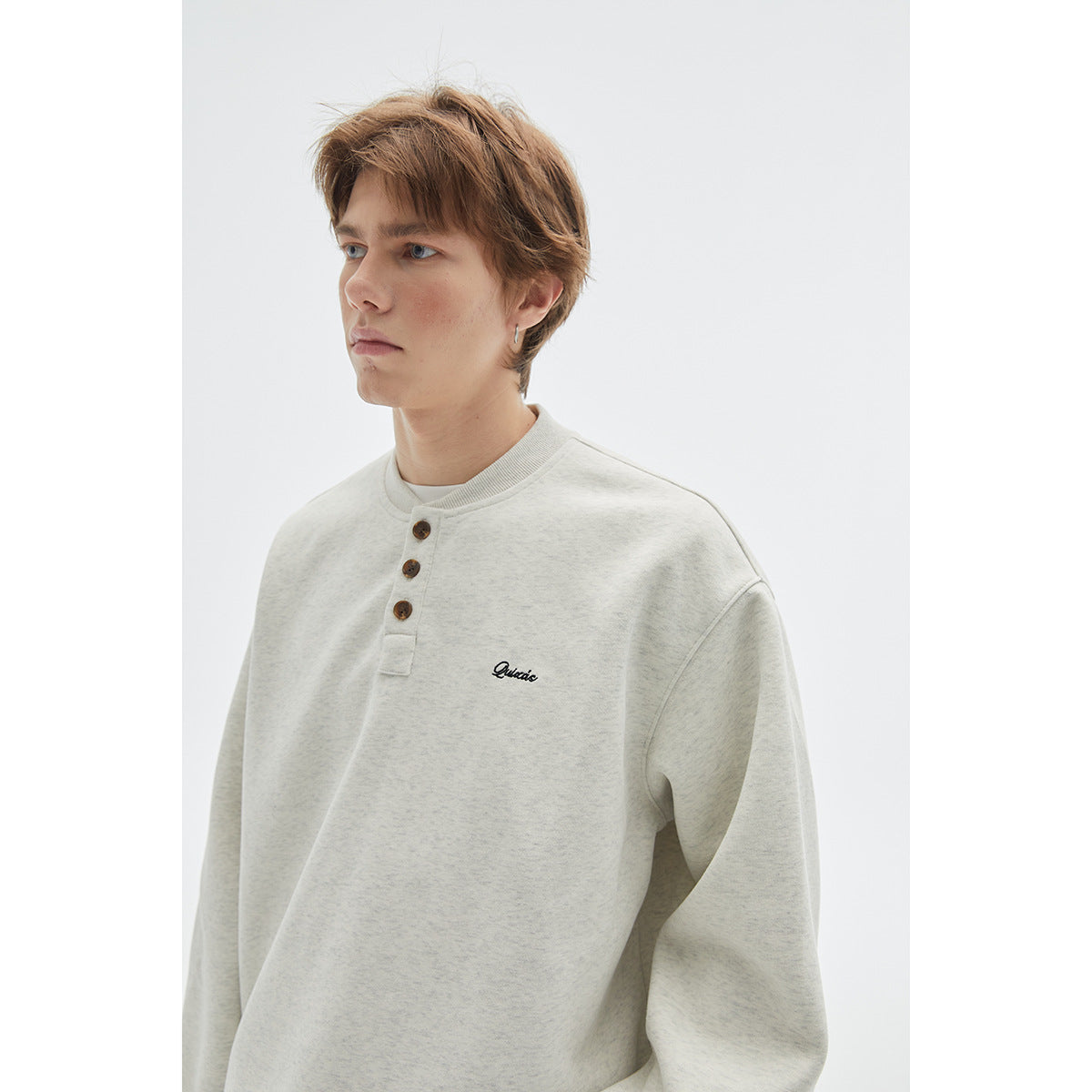 Close view of an off-white henley sweatshirt with a ribbed collar, three brown buttons, and small chest embroidery.