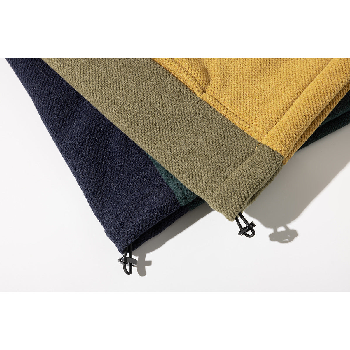 Close-up of adjustable drawcord toggles at the hems of mustard, olive, teal, and navy jackets.