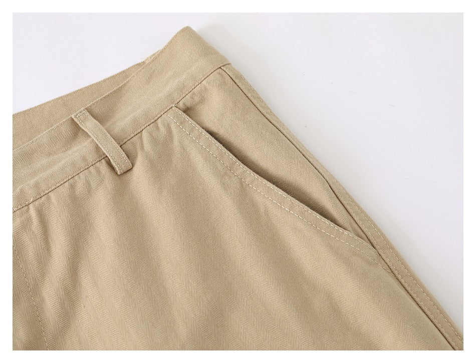 Close-up of beige pants showing a belt loop, diagonal side pocket, stitching, and subtle herringbone texture.