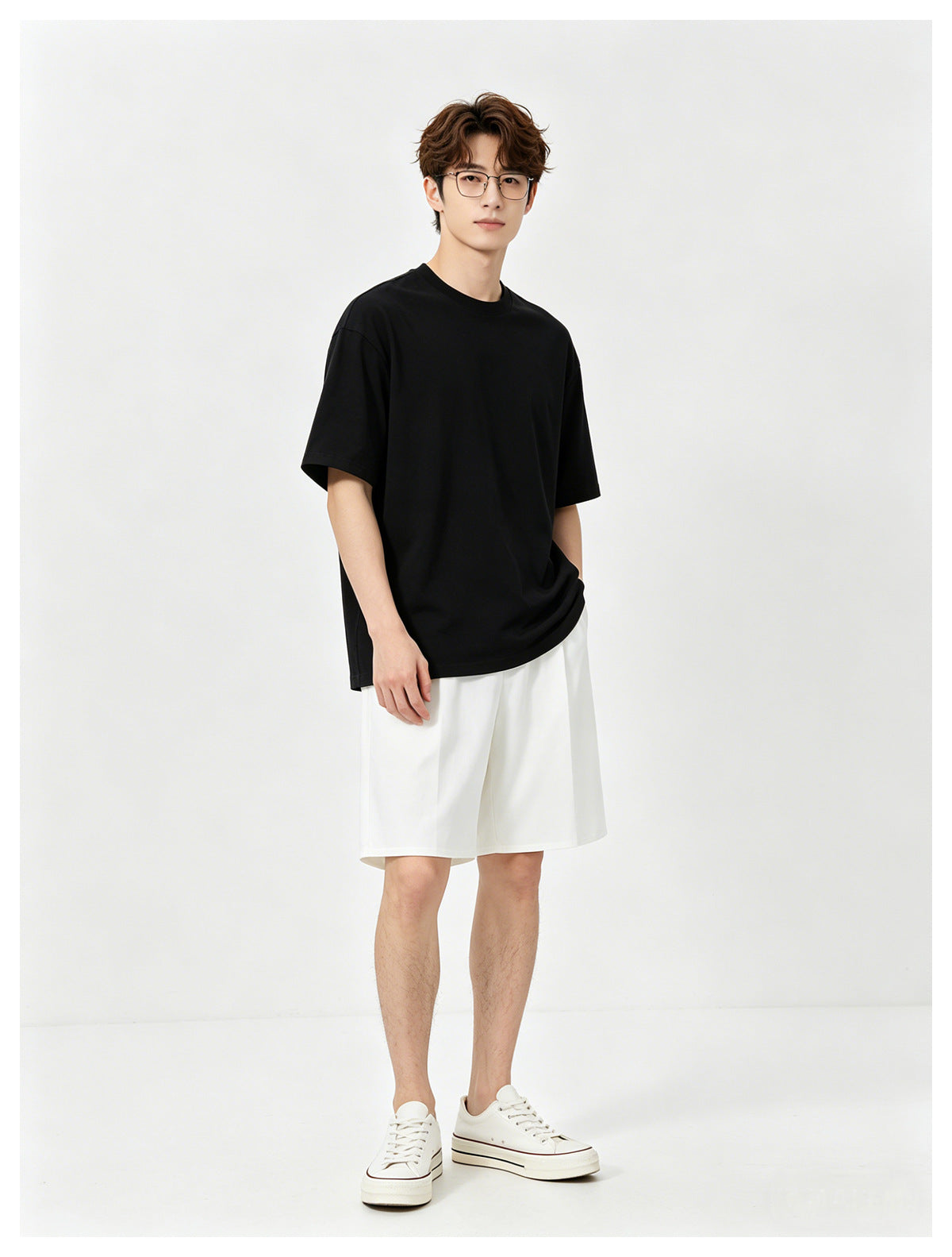 Model wearing a plain black oversized T-shirt, white shorts, and white sneakers, standing against a light backdrop.