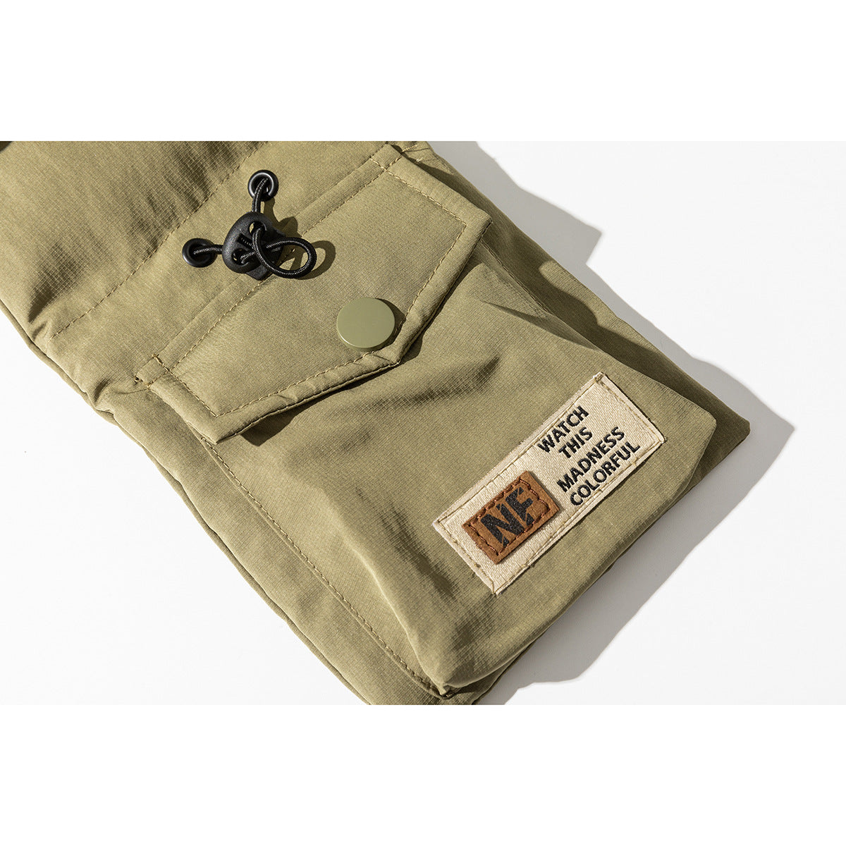 Close-up of an olive-khaki jacket pocket, snap closure, drawcord, and English text patch.
