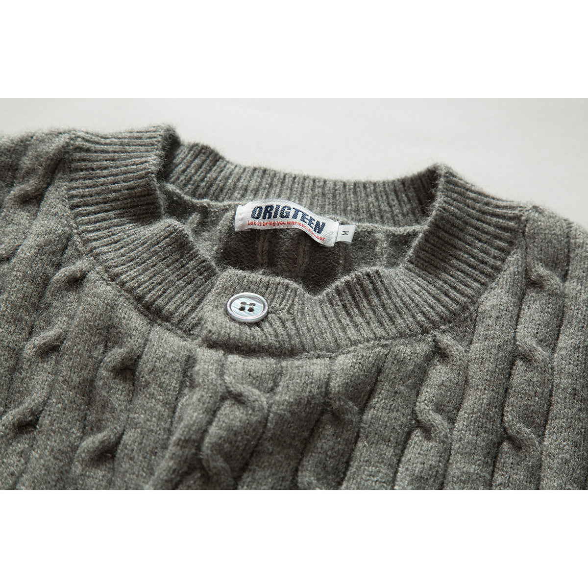 Close-up of a gray cable-knit cardigan neckline, ribbed collar, button, and sewn-in label.