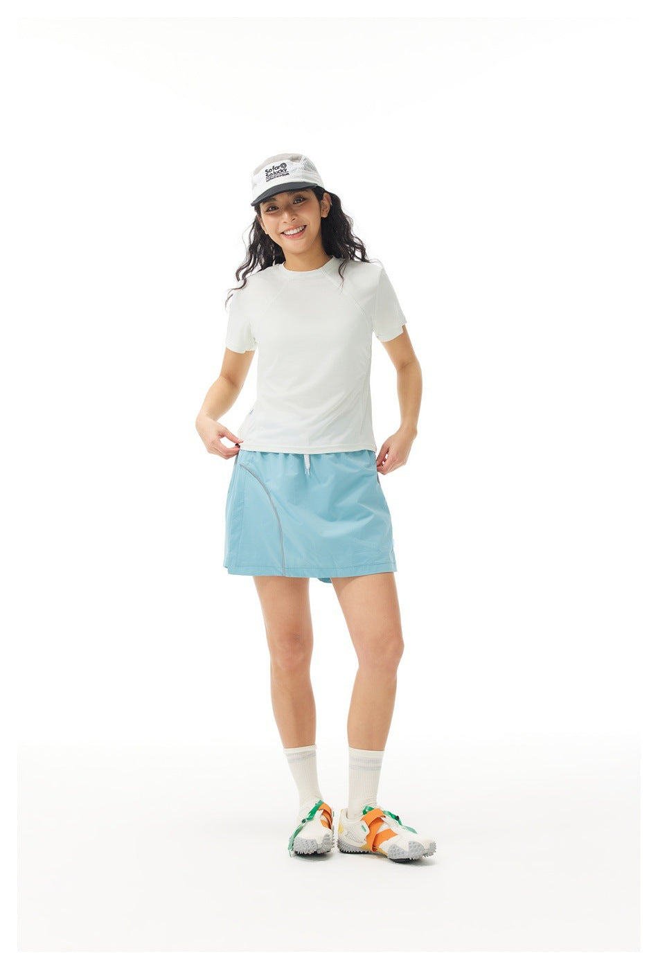 Full-length front view of a model in an off-white short-sleeve shirt and light blue athletic skirt.