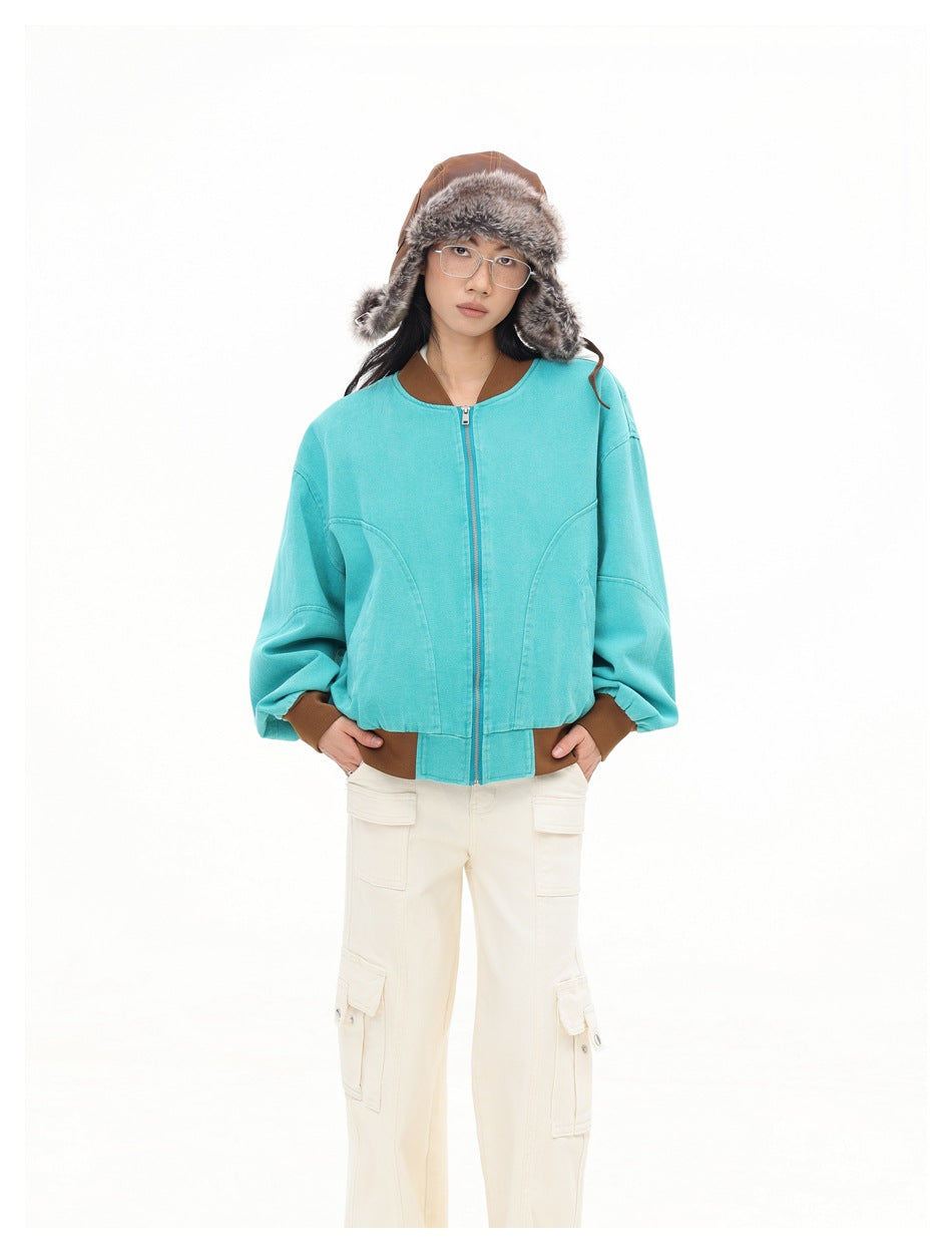 Front view of a model wearing a turquoise jacket with a center zipper, brown ribbed trim, and cream cargo trousers.