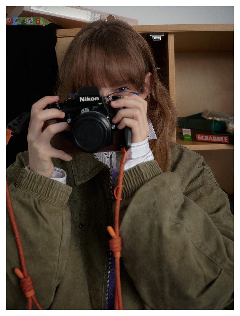 Close view of a person wearing an oversized olive jacket with a wide collar and gathered cuffs, holding a camera.