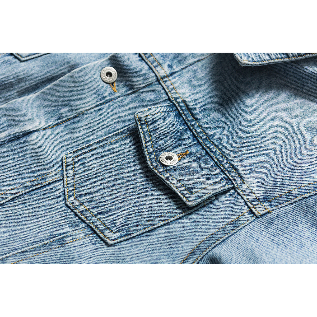 Close-up of a light blue denim jacket's buttoned flap pocket, seams and metal buttons.