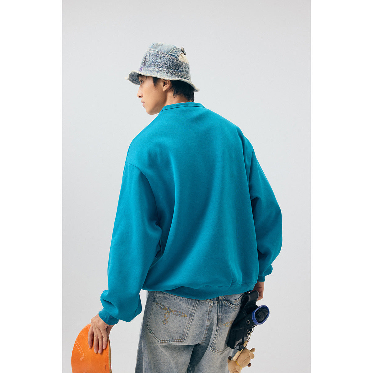 Model shown from behind in a plain teal sweatshirt with ribbed cuffs and hem.