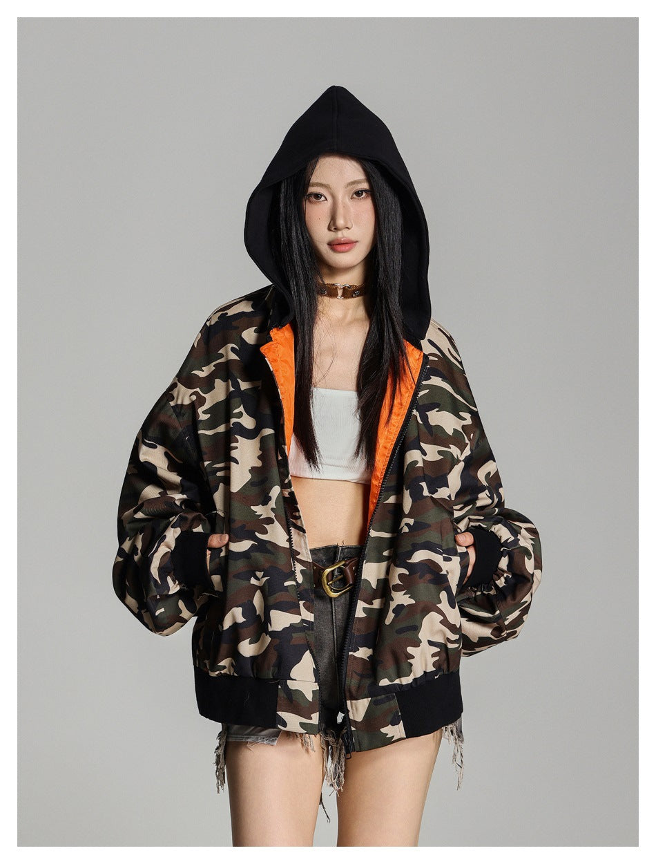 Model wearing an open camouflage jacket with orange lining, black hood and trim, shown from the front.