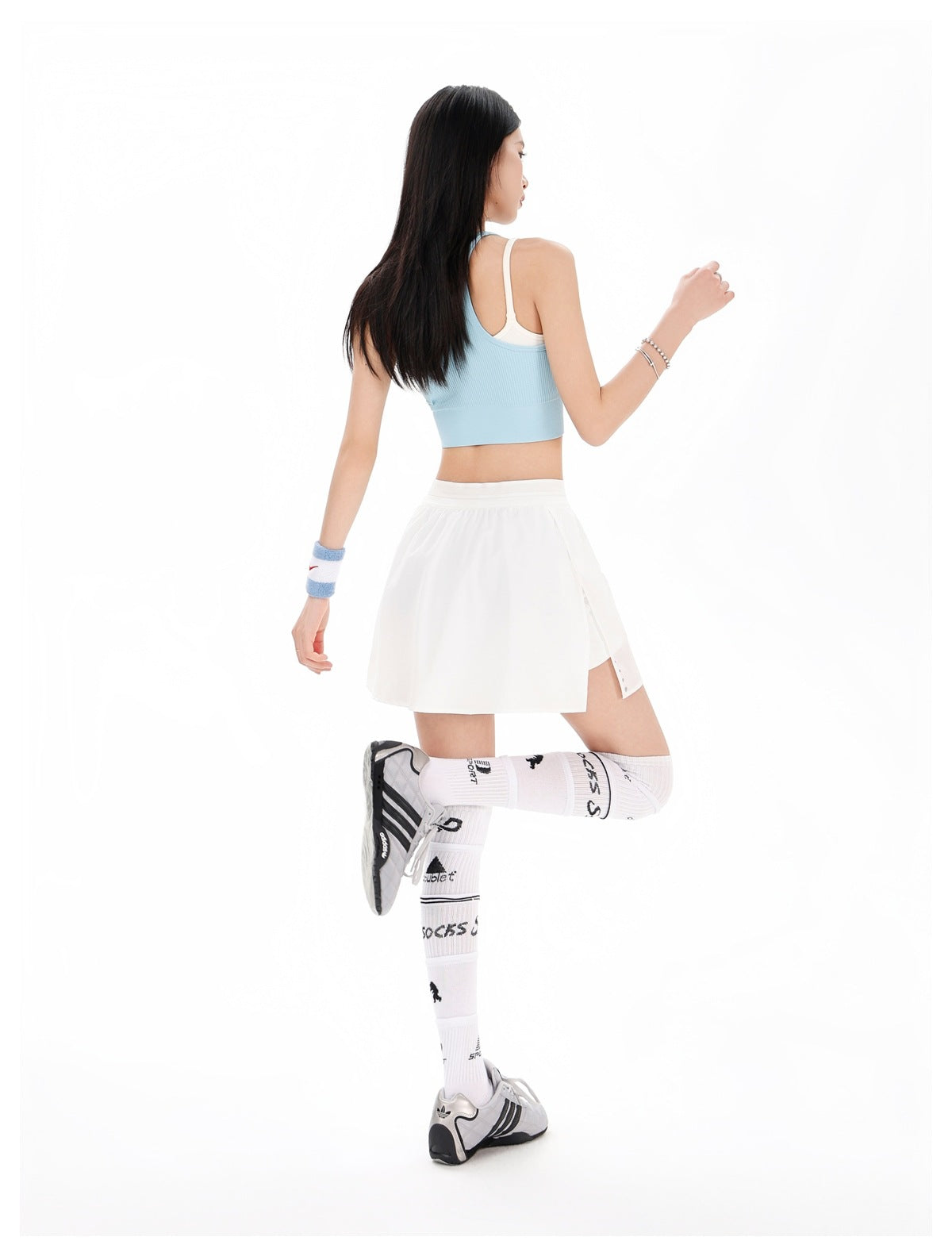 Rear view of a model wearing a white tennis skirt and pale blue sleeveless crop top.