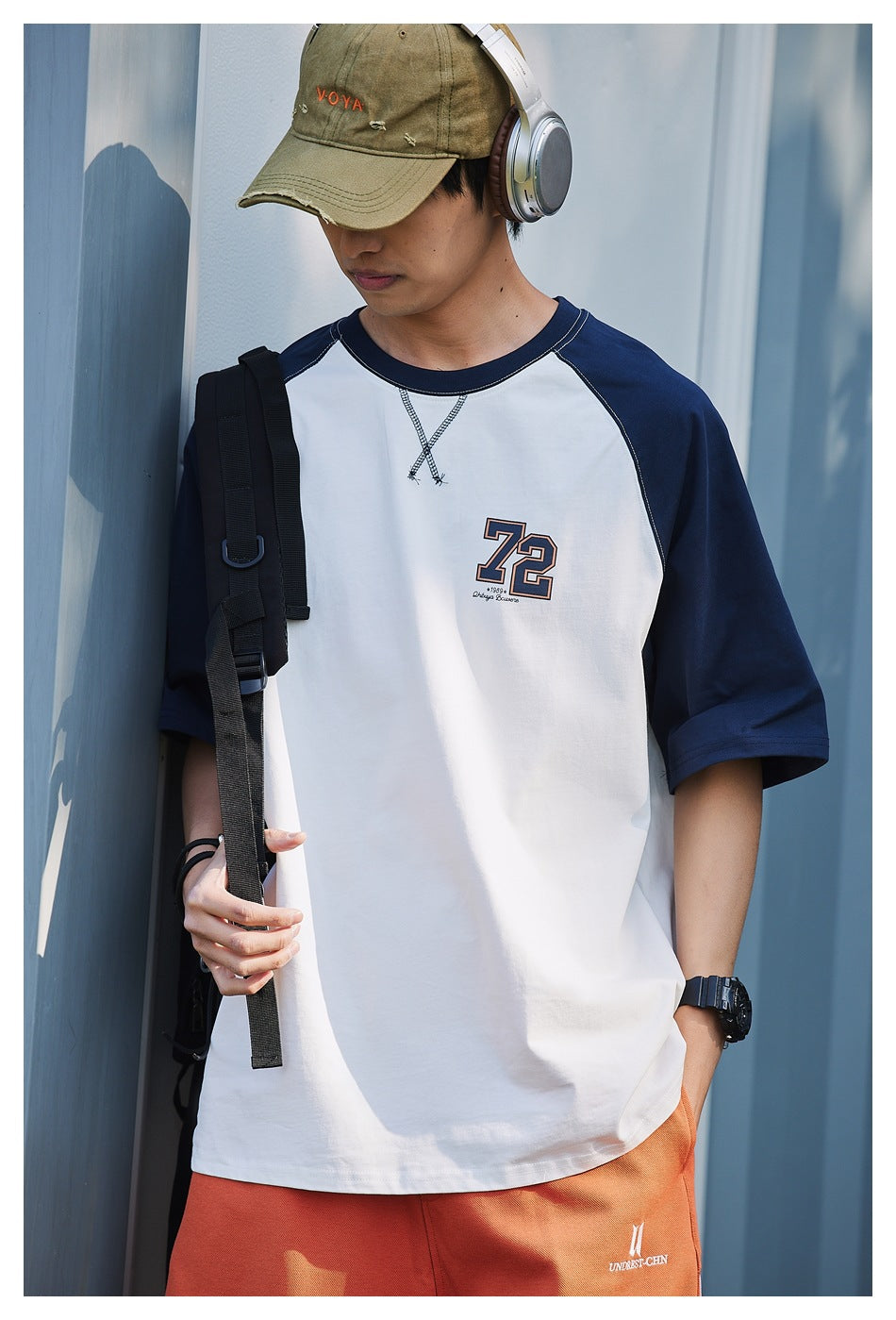 Close front view of a model wearing a white T-shirt with navy raglan sleeves and a large outlined number on the chest.