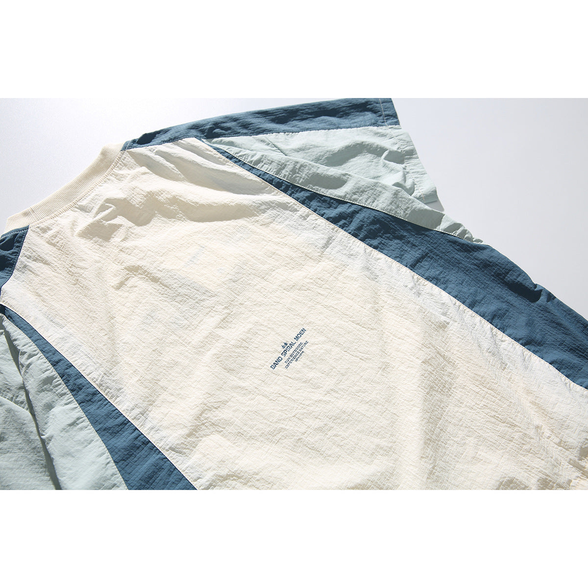 Close-up of the cream back panel of a color-block shirt with dark blue and pale blue sections and small English print.