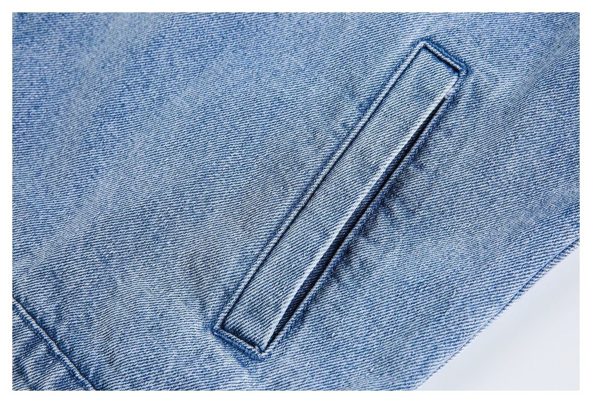 Close-up of a narrow stitched denim tab against light blue denim fabric.