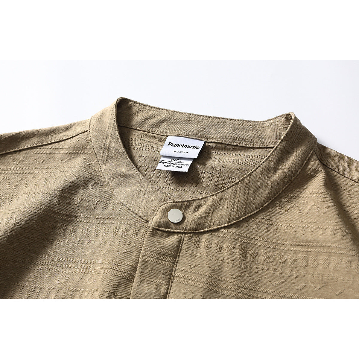 Close-up of a tan patterned shirt collar, button and placket, with a visible neck label.