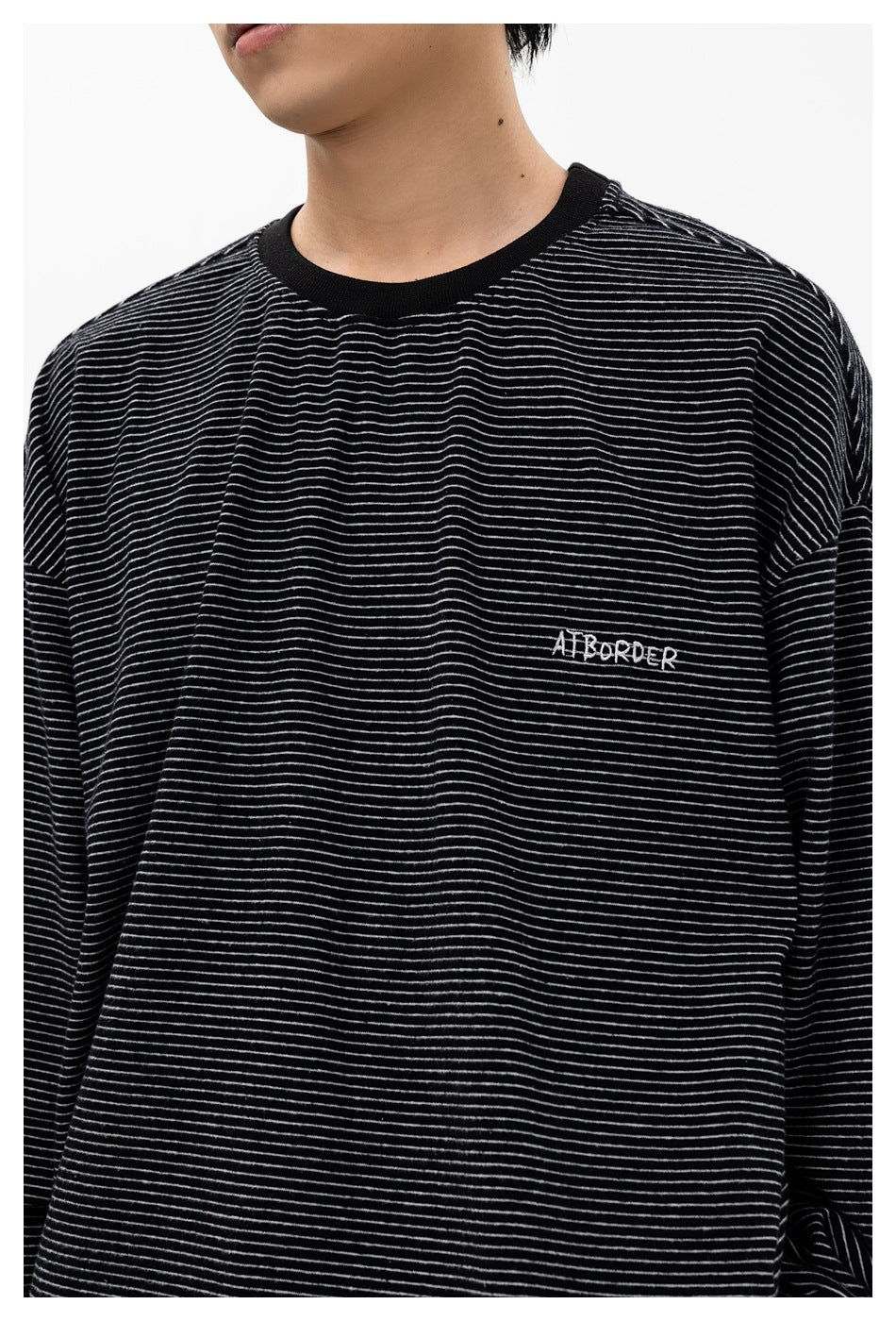 Close-up of a person wearing a black long-sleeve shirt with thin white stripes and small chest embroidery.