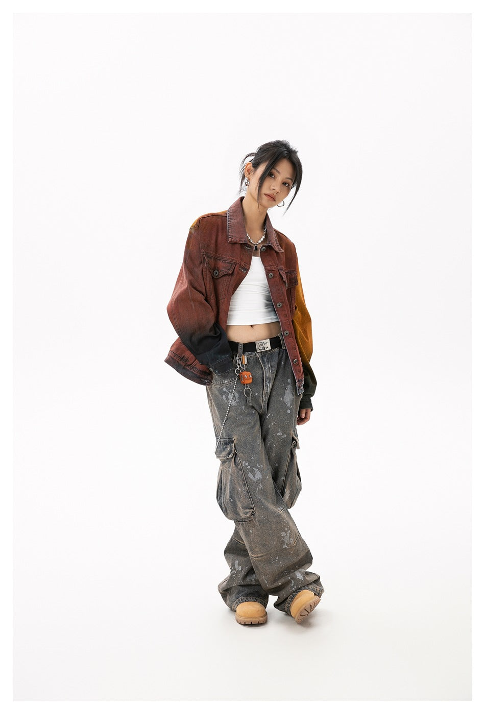 Angled full-length view of a model wearing a rust-red color-block denim jacket and distressed gray cargo jeans.
