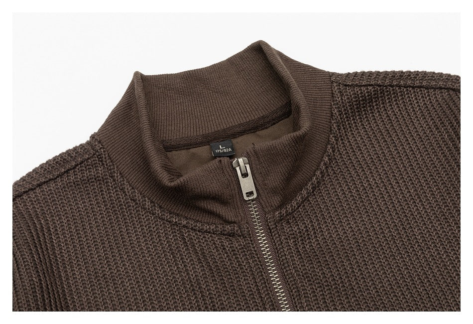 Close-up of a dark brown chunky knit sweater's stand collar, metal zipper and small size label.