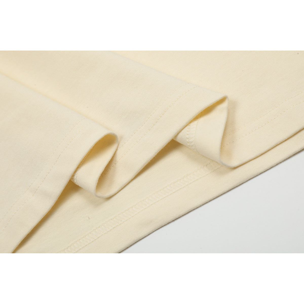 Close-up of the cream T-shirt's folded fabric and stitched bottom hem.