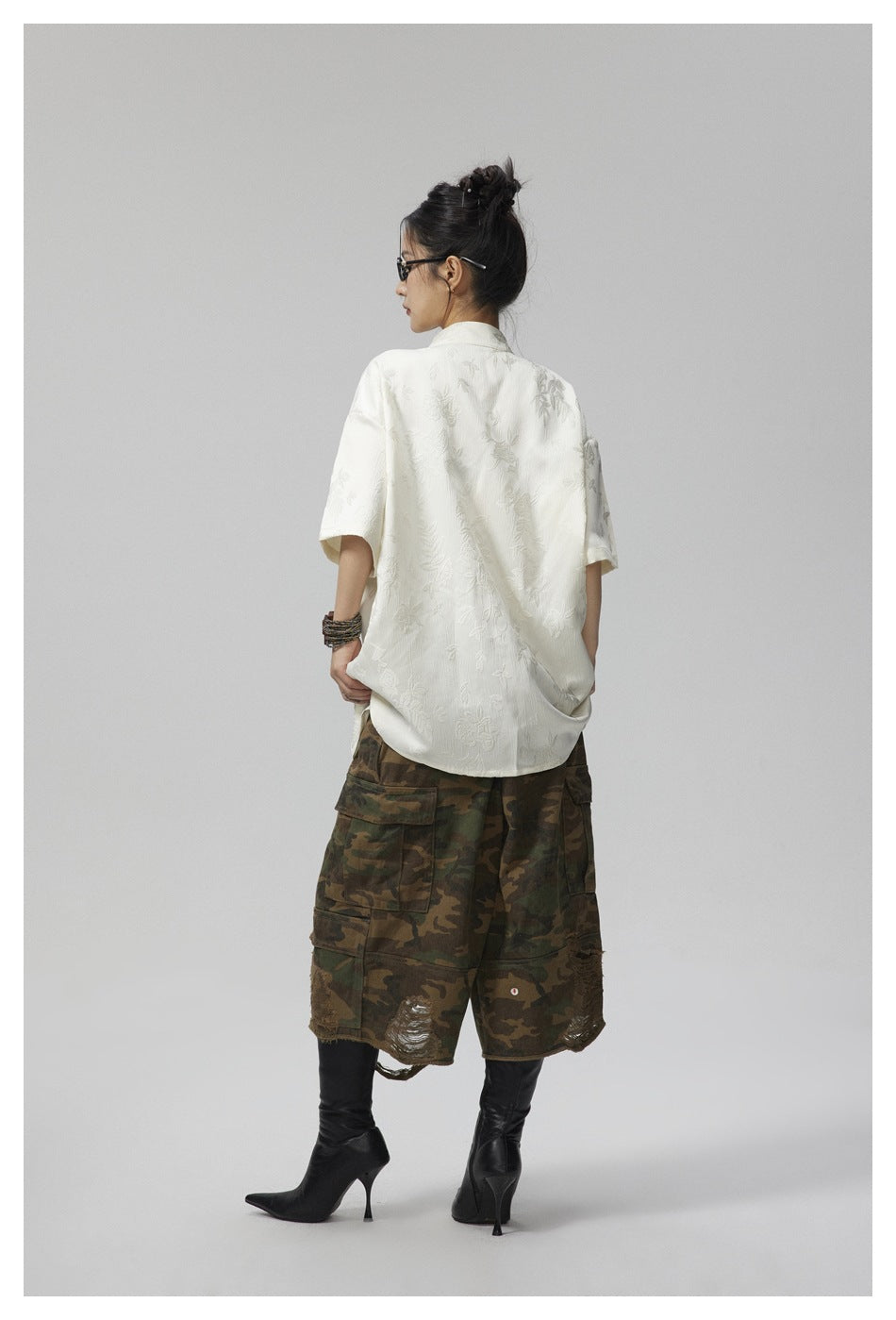 Back view of a woman wearing an off-white floral jacquard short-sleeve shirt with camo cargo shorts and black boots