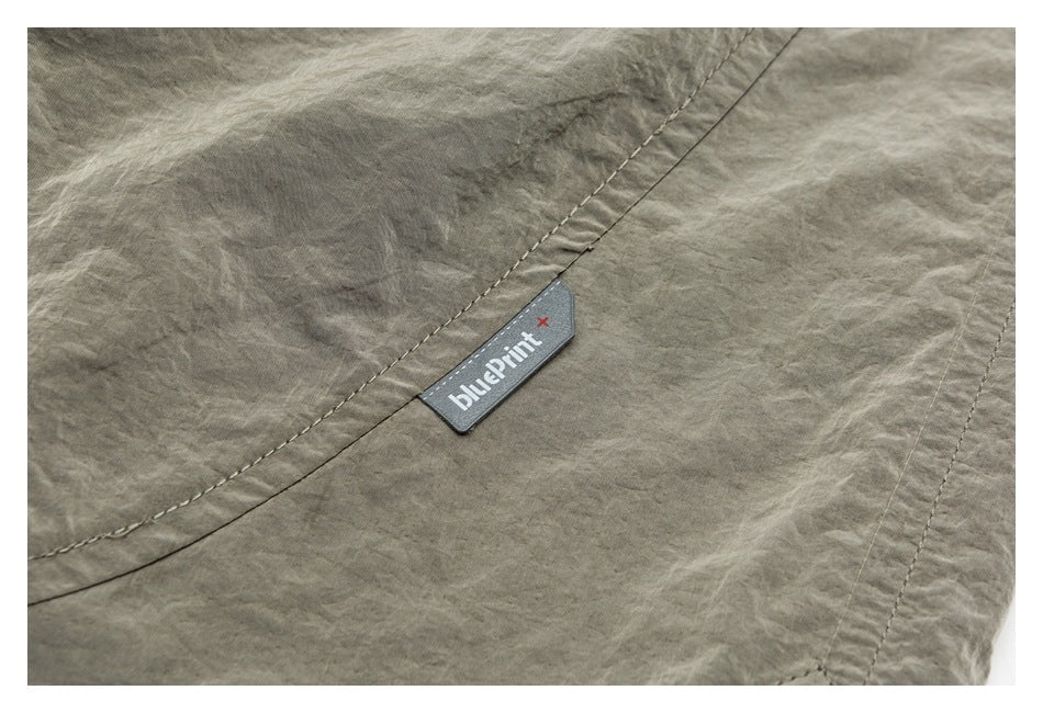 Close-up of a gray-green garment with curved stitching and a sewn Blueprint+ label.