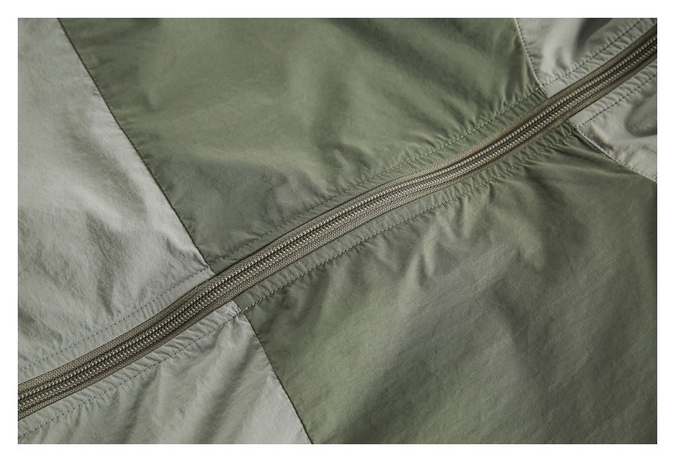Close-up of a diagonal zipper crossing sage green and pale gray color-block panels.