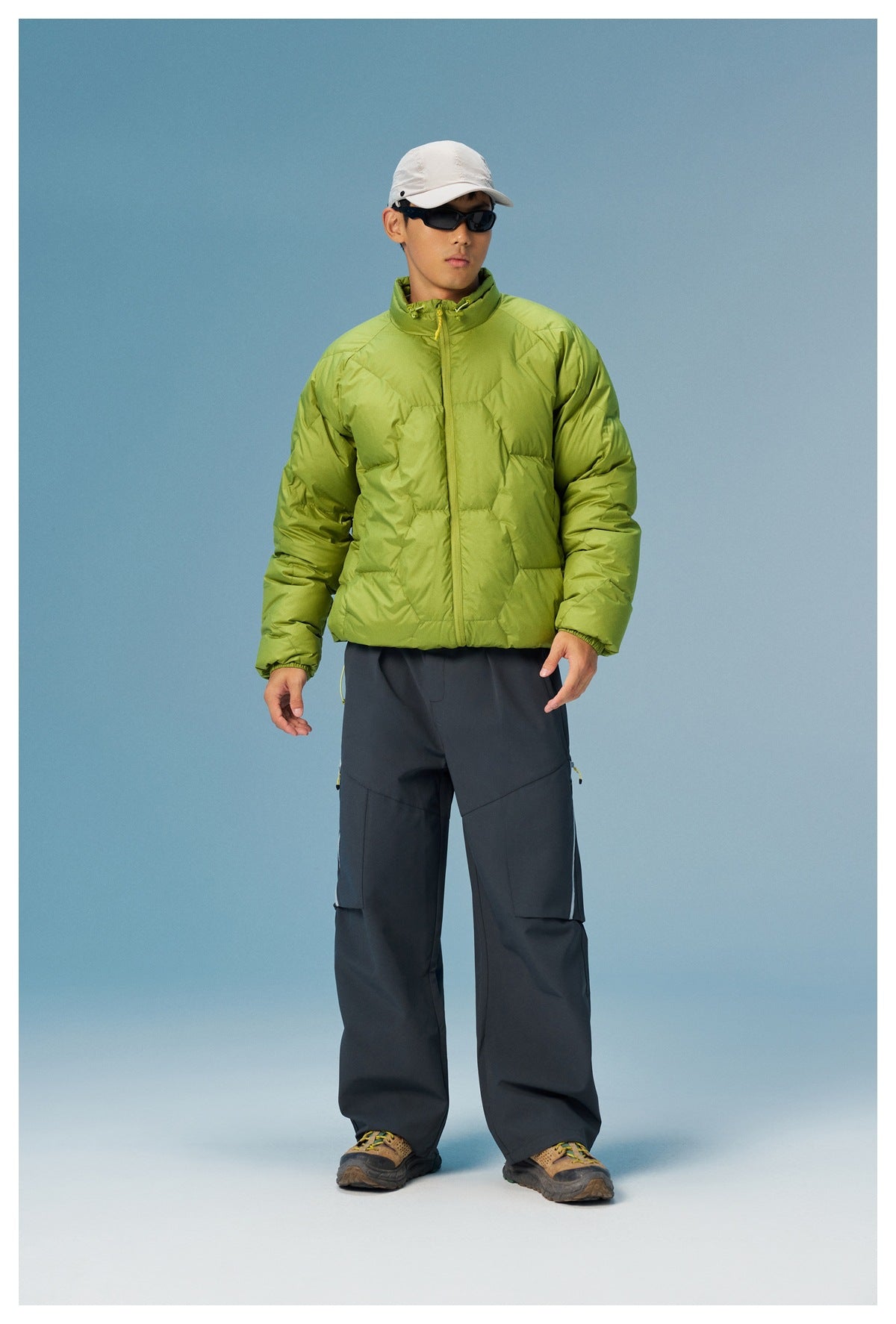 Model in a lime-green quilted zip jacket and dark cargo pants, standing full length against a blue background.