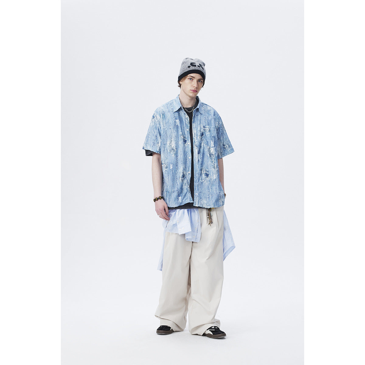 Full-length front view of a model wearing a blue distressed-pattern short-sleeve shirt and loose cream trousers.