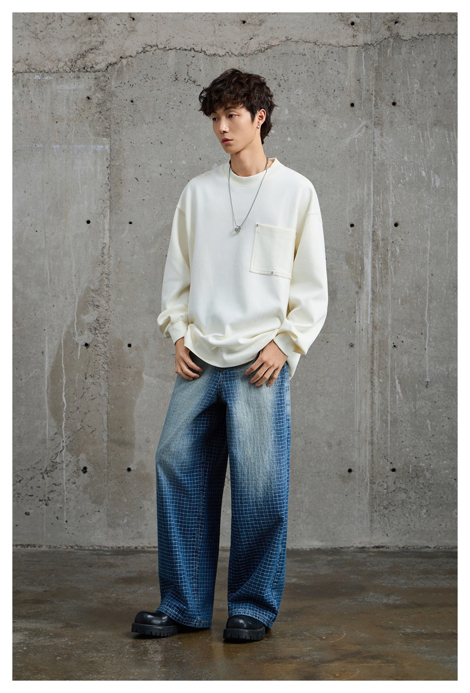 Full-length view of a model wearing an oversized ivory pocket sweatshirt, wide-leg blue checked trousers, and black shoes.