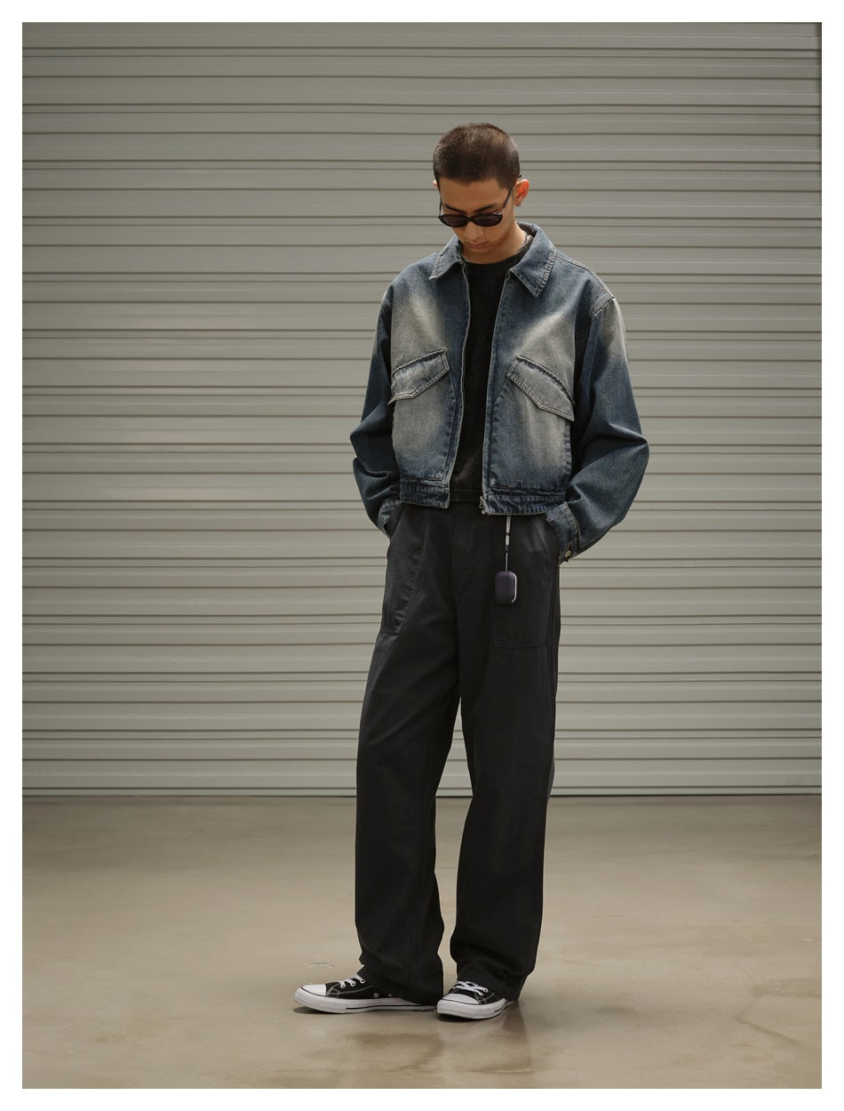 Model wearing a cropped, faded blue denim jacket with flap chest pockets and loose black trousers.