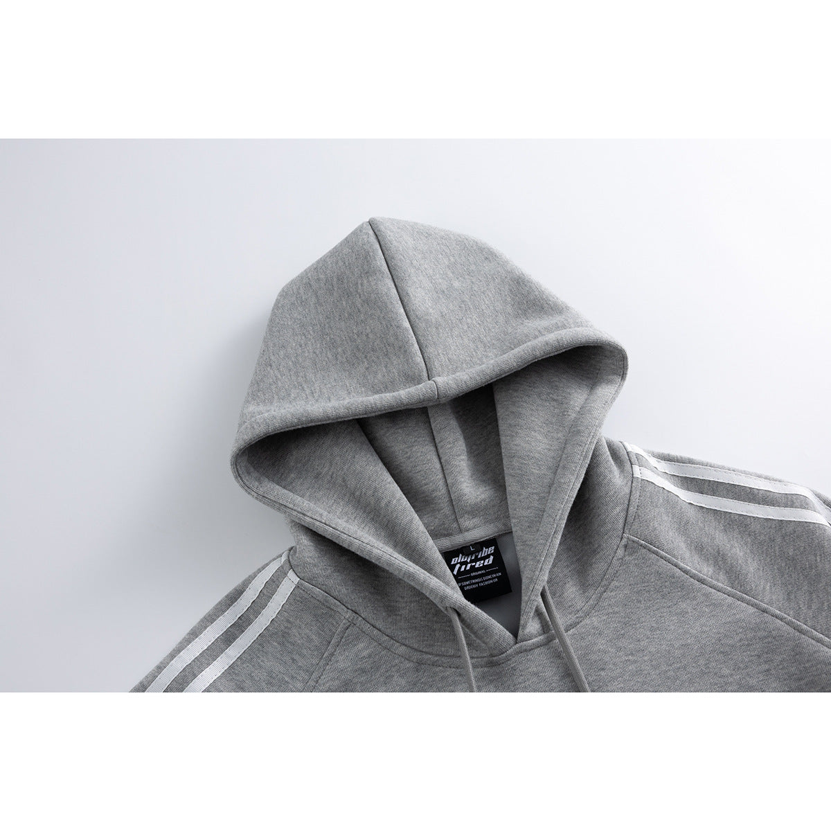 Close-up of a gray hoodie showing its hood, drawstrings, white shoulder stripes, and inner neck label.
