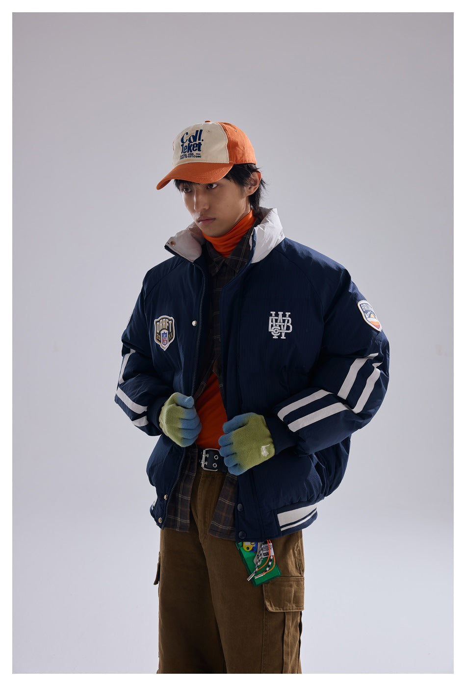 Model wearing a navy puffer jacket with a white collar, sleeve stripes and chest patches, shown from the front.