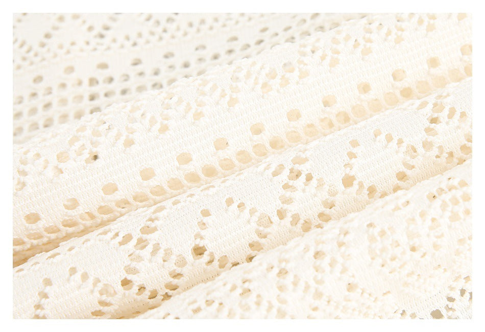 Close-up of ivory lace fabric showing rows of openwork holes and floral stitching.